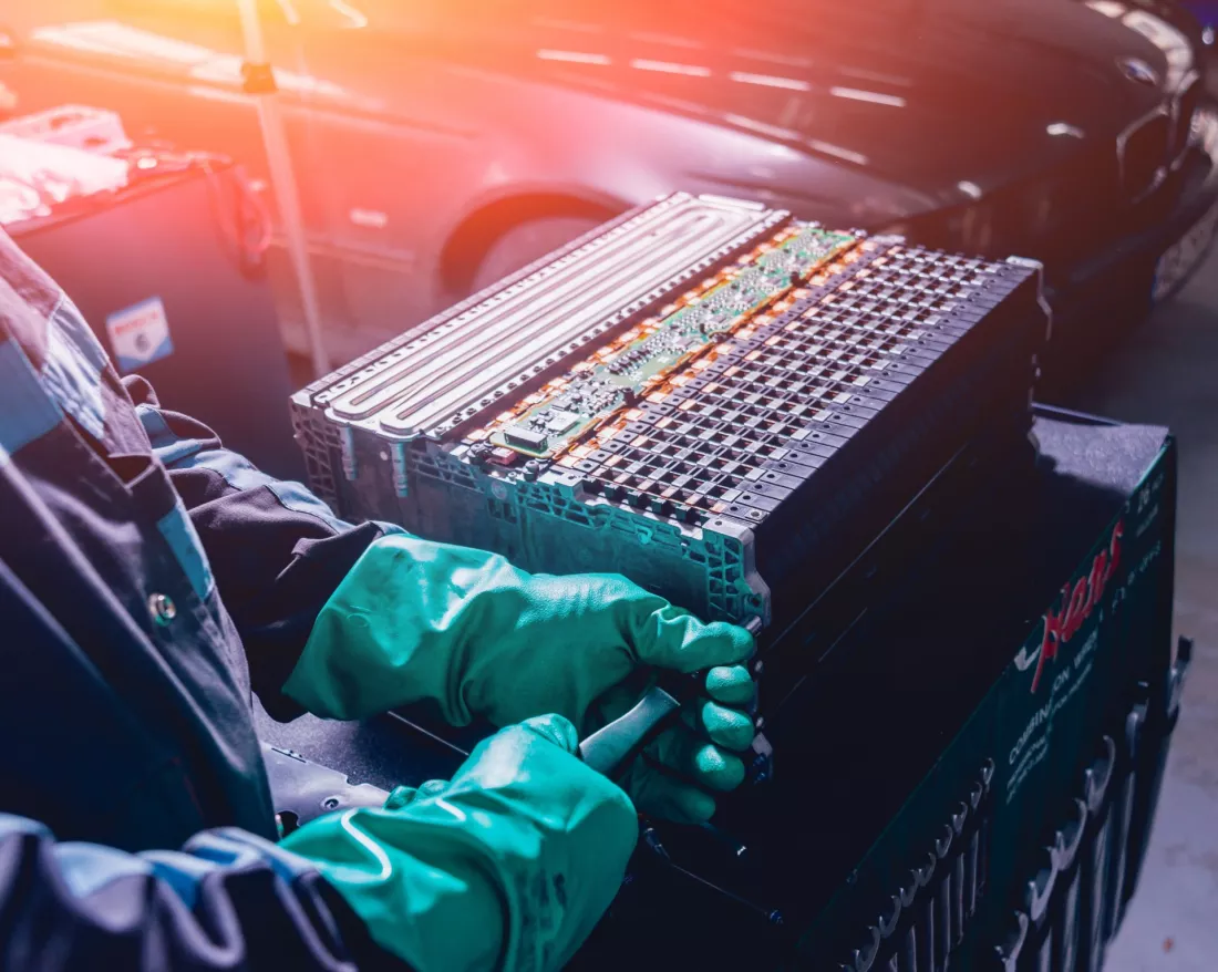 Mani con guanti smontano il pacco batteria di un auto elettrica
