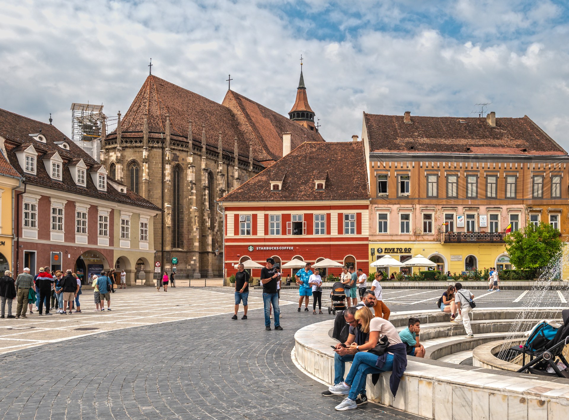 Giovani che si rilassano accanto alla fontana in Piazza del Consiglio a Brașov, con la Chiesa Nera sullo sfondo